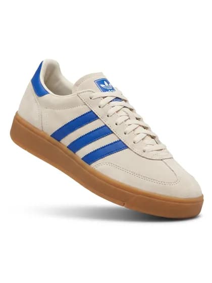 A cream suede low-top sneaker with blue stripes and a gum sole, shot on white.